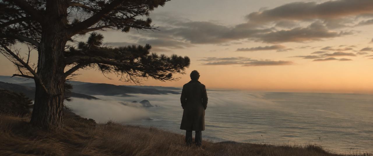 A figure in a wool overcoat standing at the edge of a coastal bluff at dusk, looking out over the Pacific